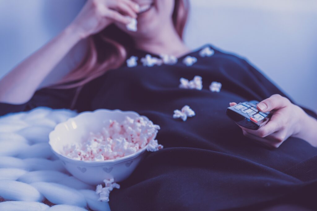 Women eating popcorn and watching tv because she is suffering with procrastination